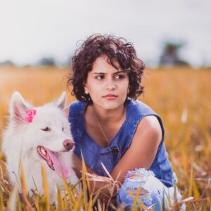 Woman Squatting Near White Dog on Grass Field