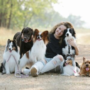 Gentle smiling woman embracing purebred dogs while sitting on ground