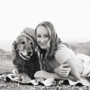 grayscale photography of smiling girl lying on textile beside golden retriever