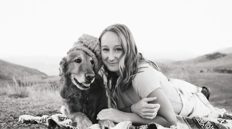 grayscale photography of smiling girl lying on textile beside golden retriever