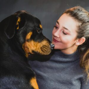 woman in black crew neck shirt hugging black and tan short coat dog