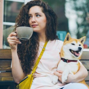 a woman sitting on a bench holding a cup and a dog