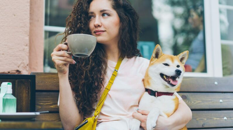 a woman sitting on a bench holding a cup and a dog